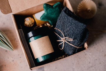 Christmas box with presents - candle in dark jar, chocolate candies, cozy grey socks and festive...