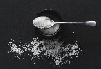 Organic sea white salt, jar and a spoon on a black slate background. Concept of cooking natural healthy food