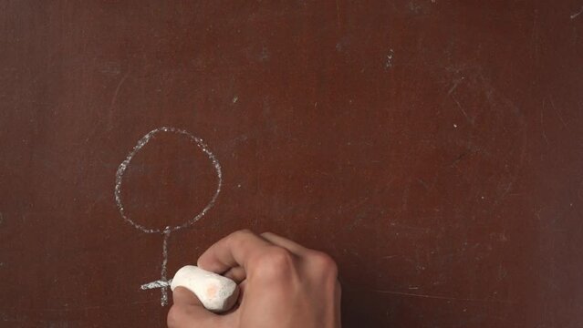 Textured brown chalkboard background. Male hand drawing female and male gender symbols on the board with a piece of white chalk in close up.