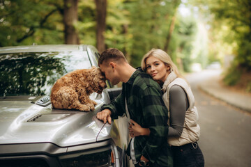 happy couple with pet dog cocker spaniel on a walk in the autumn forest near the car