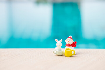 Snowman with white rabbit and coffee cup on swimming pool edge, outdoor day light, Christmas...