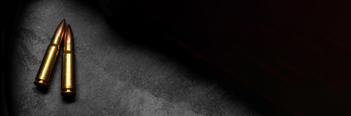 Two bullets for Kalashnikov assault rifle on gray concrete and gradient black background banner. Cartridge 7.62 caliber for ak 47 panoramic web header. Wide screen wallpaper - obrazy, fototapety, plakaty