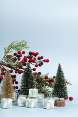 Composition with colorful gifts, a branch of holly with its red berries and christmas tree against a luminous sky-blue background.