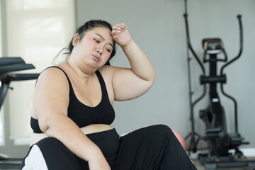 Exhausted young Asian woman after workout in fitness club. Young overweight woman hard work to lose...