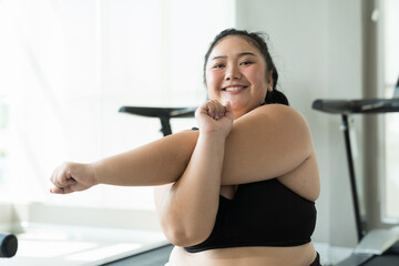 Happy Asian young chubby size woman in sportswear stretching arms in fitness club. Young overweight woman warm up training before workout at gym. Workout sport concept - obrazy, fototapety, plakaty
