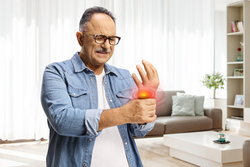 Mature man suffering from arthritis and holding his painful wrist - obrazy, fototapety, plakaty