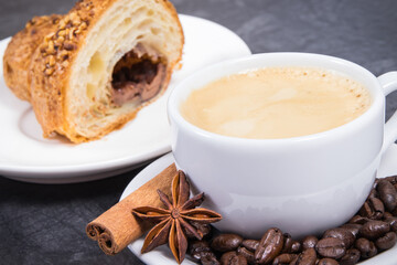 White cup of coffee with seasonings and fresh croissant with chocolate