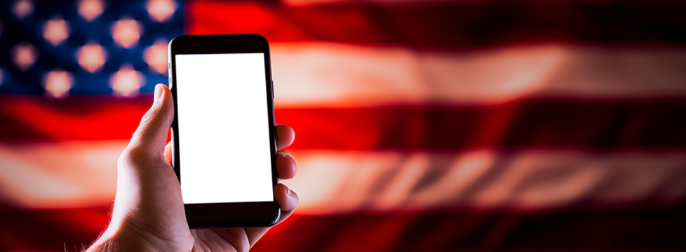 Hand holding a Smartphone with transparent cut out set against the stars and stripes, flag of the USA. shallow field of view.