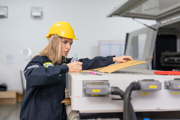 Female engineer checking quality cardboard box parts cutting from laser CNC machine in paper factory. Woman technical in uniform wearing helmet safety operate and maintenance machine