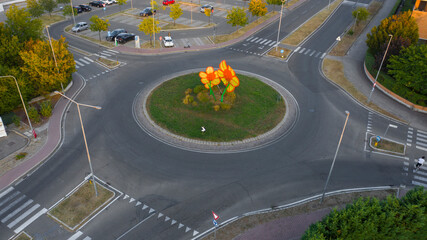 Aerial view of a large roundabout with large orange flowers in the middle. On the road there are no...