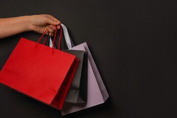 Big sale, low prices. Female hand holds colored paper shopping bags on black background, copy...