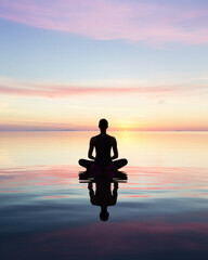 woman silhouette meditating in lotus position in a timeless space, horizon with a soft and colorful sky reflected on the water, sunset and pastel sky color with blue pink and orange  - obrazy, fototapety, plakaty