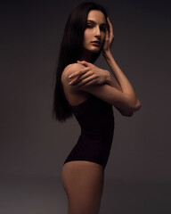 A beautiful young girl in a black bodysuit with long sleeves stands on a dark background.