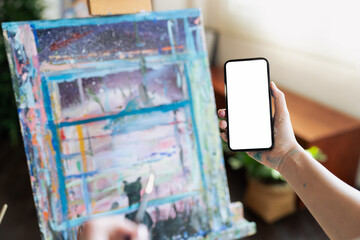 Designer or Artist holding blank screen smartphone over canvas of an artist with art