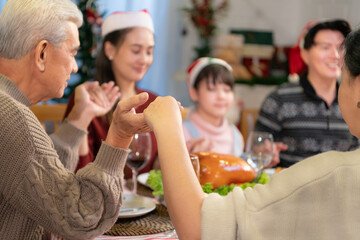 Young asian man praying with his family during Christmas dinner at home