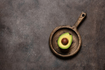 Half an avocado on a wooden plate, dark rustic background. Top view, flat lay.