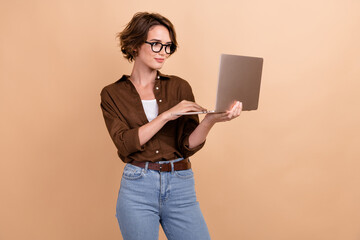 Photo of positive confident girl dressed brown shirt eyewear working modern gadget isolated beige color background