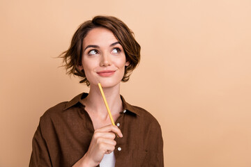Photo of dreamy pretty girl dressed brown shirt holding pencil looking empty space isolated beige...