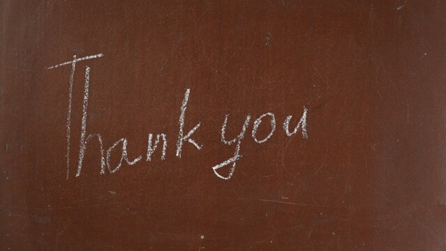 Textured brown chalkboard background. 'Thank you' is written on the board with a piece of white chalk. Close up shot.