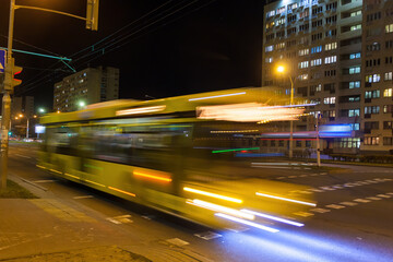 A blurry bus moves along the avenue in the evening.