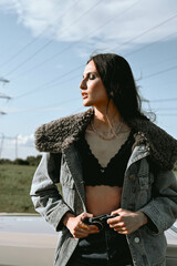 A beautiful woman stands next to a convertible in a field. Dressed in jeans and a jacket with fur. Beautiful and stylish look