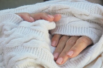 Female hands with natural manicure on the background of a white knitted wool scarf. Hand care, professional salon manicure.