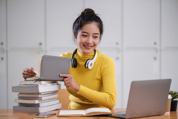 Young adult asian student woman taking notes while using laptop computer at home. Asian female learning online listening virtual video call. Business and education concept.