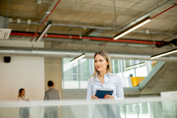 Young woman with notebook standing in the modern office hallway