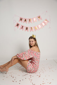 birthday photo of a young girl on a white background. short pink party dress. a crown on the birthday girl's head. pink inscription happy birthday. The girl is 16 years old. fashionable young woman