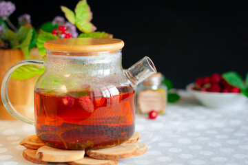 A transparent teapot filled with bright berry-herbal healing tea, standing on a hot stand made of wood cuts, a bright light still life