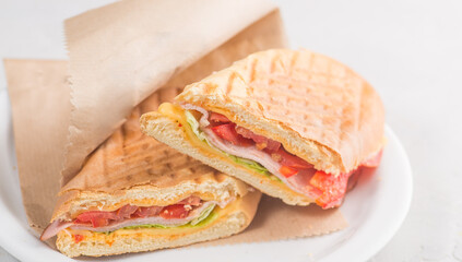 Sandwich with ham, cheese and tomatoes. Sandwich with sauce in a grilled white bun.