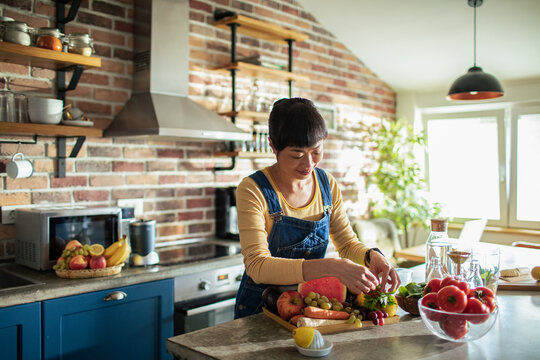Focused Asian Woman Preparing Fresh Organic Ingredients in Sunlit Kitchen