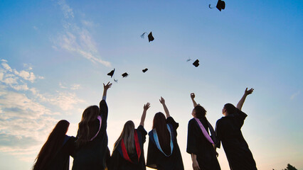 Silhouettes of graduates toss their caps at sunset.