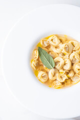 Italian ravioli with aromatic broth and sage leaf in a white plate. Close-up,  top view. Italian traditional winter and holiday cuisine