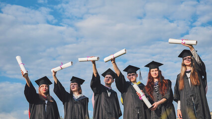 Cheerful graduates pose with raised diplomas on a sunny day.