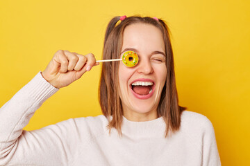 Caucasian adult smiling woman covering her eye with lollipop isolated over yellow background...