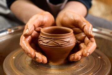 Fototapeta na wymiar Pottery wheel. Artisan's creation. Dirty form. Handicraft skill. Clay work. Potter's hands gently and surely formed by clay pot on potter's wheel.