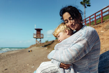 Mom is hugging her three-year-old son on the seashore.