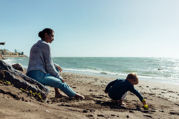 A young mother and her three-year-old son run, play, smile, and laugh on the seashore.