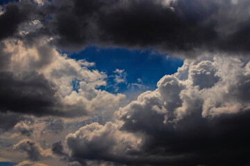 Obraz premium patch of blue sky, framed by shadowy cumulus clouds.