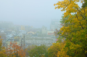 Picturesque aerial landscape view of ancient Podil neighborhood during fog. Mysterious cityscape. Kyiv during autumn thick fog. Tree leaves boarder, natural composition