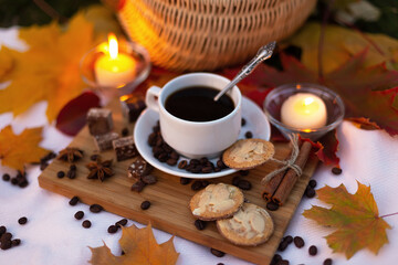 Evening picnic by candlelight with coffee, cookies and chocolate in autumn park with maple leaves. Still life. Food outdoors in garden.