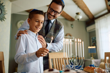 Happy boy lights menorah with his father on Hanukkah at home.