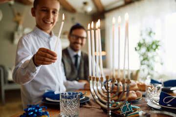 Close up of boy lights candles in menorah while celebrating Hanukkah with his father at home.