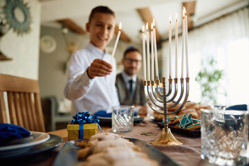 Close up of Jewish kid lights menorah during Hanukkah celebration.