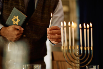 Close up of Jewish man lights candles in menorah while celebrating Hanukkah at home.