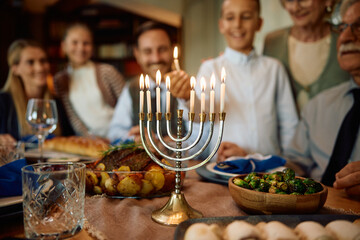 Close up of Jewish kid lights candles in menorah during family gathering on Hanukkah.