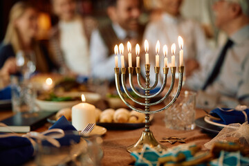 Lit candles in menorah with extended Jewish family in background on Hanukkah.