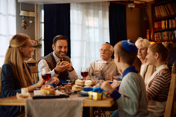 Happy Jewish man communicating with his extended family at dining table on Hanukkah.