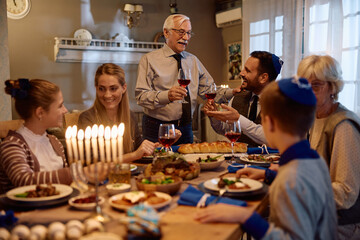 Happy Jewish father and son toasting during Hanukkah family celebration in dining room.